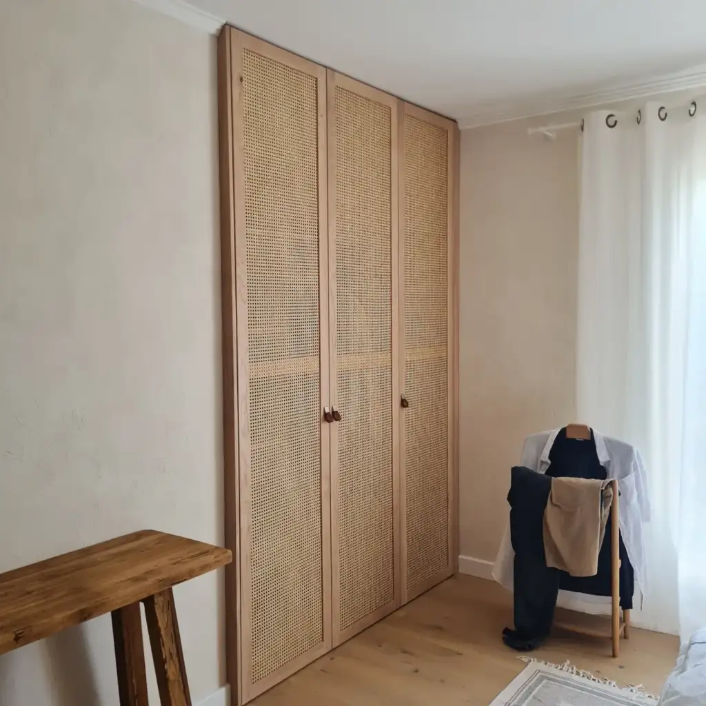 Dressing sur mesure avec portes en cannage et bois clair Armoire encastrée en bois clair avec portes en cannage rotin dans une chambre lumineuse au style minimaliste.
