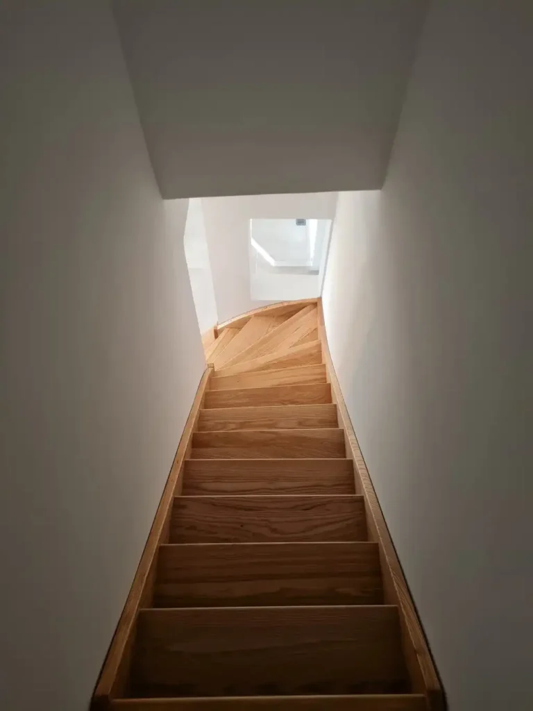 Escalier en Bois Moderne et Design Intérieur Minimaliste Escalier étroit en bois clair au design épuré menant vers un palier lumineux sous un puits de jour.