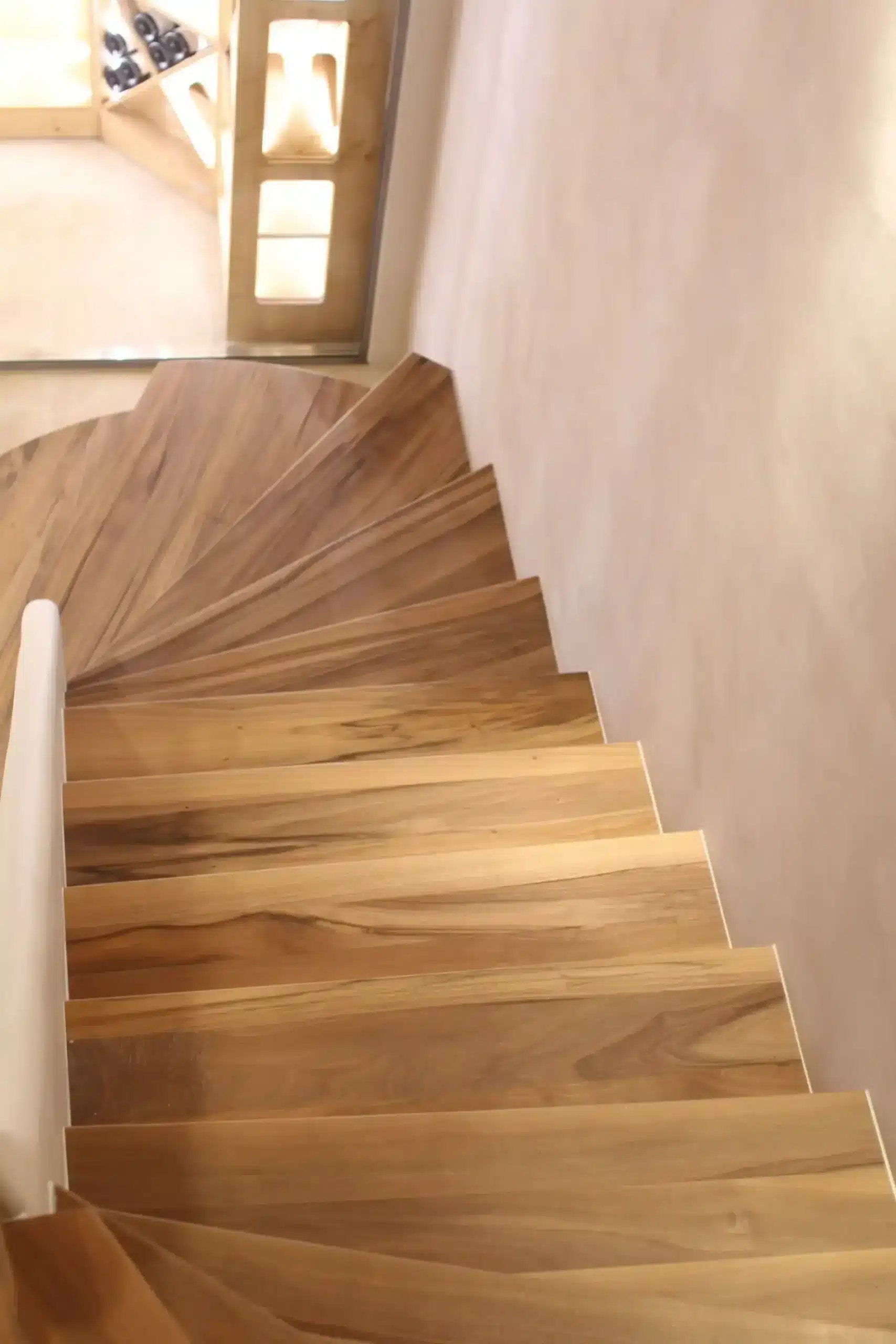 Vue plongeante d'un escalier en colimaçon en bois de noyer avec rampe blanche et mur épuré.