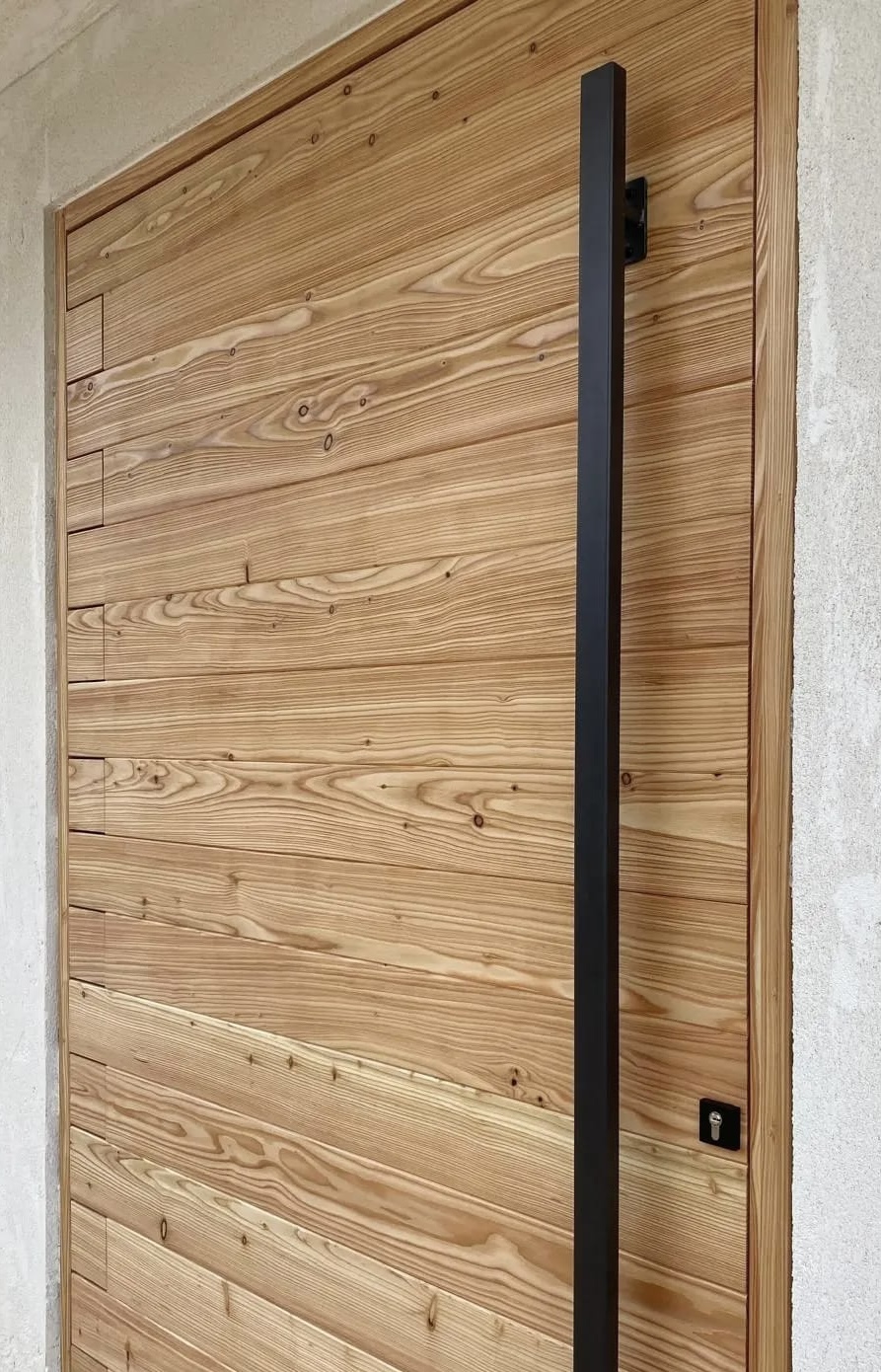 Porte d'entrée sur pivot invisible en bois de mélèze et poignée en acier