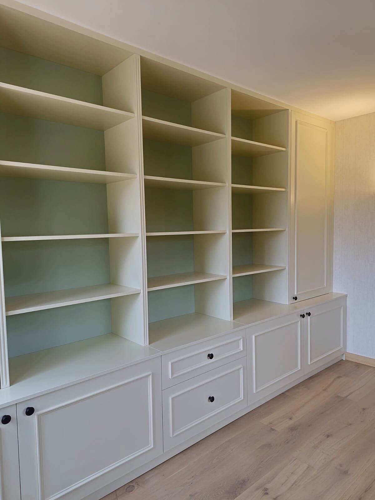 Meuble de rangement sur mesure en laque crème avec fond vert ouvert, installé dans une maison à Mougins, lignes épurées et esthétisme raffiné