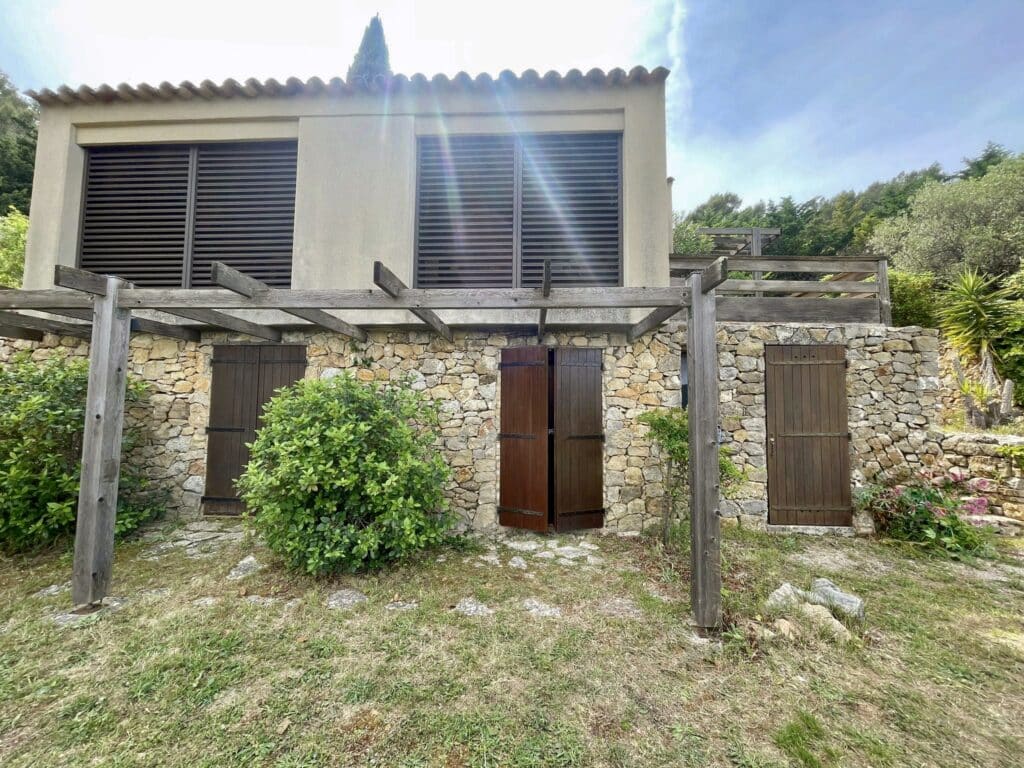 Maison provençale en pierre avec volets bois, pergola rustique et jardin méditerranéen ensoleillé.